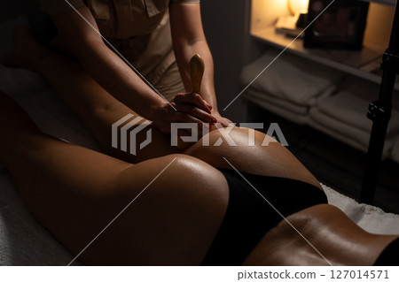 Anti-cellulite massage on the stomach using wooden objects. Massage salon in a dark room. Anti-cellulite massage on the stomach using wooden objects. Massage salon in a dark room. 127014571
