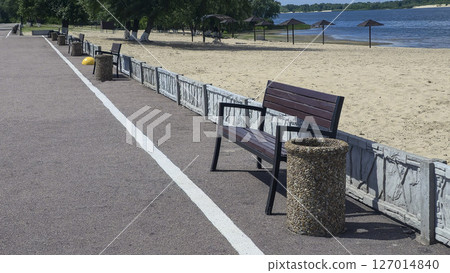 Wooden benches and trash bins line the side of the road in a park recreation area Wooden benches and trash bins line the side of the road in a park recreation area 127014840