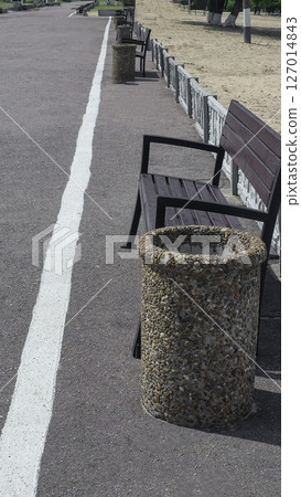Wooden benches and trash bins line the side of the road in a park recreation area Wooden benches and trash bins line the side of the road in a park recreation area 127014843