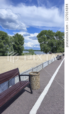 Wooden benches and trash bins line the side of the road in a park recreation area 127014844