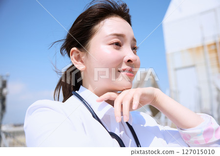 A female doctor looking up at the sky on the hospital roof 127015010