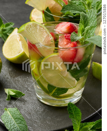 Refreshing mojito cocktail with lime, mint, strawberry, and ice on dark background Refreshing mojito cocktail with lime, mint, strawberry, and ice on dark background 127015886