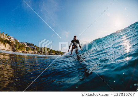 Surfer on a powerful wave near tropical cliffside beach on a sunny day. Action and adventure lifestyle. 127016707