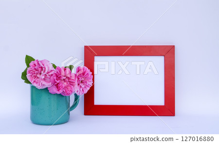 Rose flowers in a mug and red wooden frame with empty space on a white background. Rose flowers in a mug and red wooden frame with empty space on a white background. 127016880