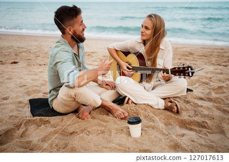 Romantic Couple Smiling on Beach While Girl Plays Guitar at Sunrise 127017613