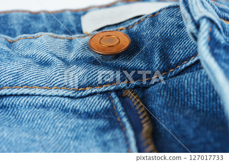 Close-up of denim jeans button and zipper, detailed view of textile, stitching, and copper hardware Close-up of denim jeans button and zipper, detailed view of textile, stitching, and copper hardware 127017733