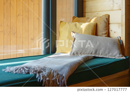 Cozy seating area with decorative cushions and blanket by large window sill in wooden room Cozy seating area with decorative cushions and blanket by large window sill in wooden room 127017777