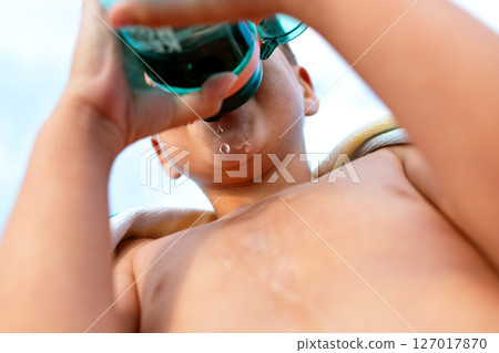 Boy drinking water from a bottle on a summer day at the beach, seen from below. Boy drinking water from a bottle on a summer day at the beach, seen from below. 127017870