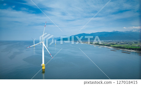 A view of the humid coast of Toyama Prefecture, Japan, with its surrounding offshore breakwaters and offshore wind turbines during the rainy season. 127018415