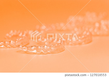 Orthodontic silicone aligner background. Advertisement of invisible braces retainer. Medical website concept. Pros and cons of aligners. peach saturated background Orthodontic silicone aligner background. Advertisement of invisible braces retainer. Medical website concept. Pros and cons of aligners. peach saturated background 127018553