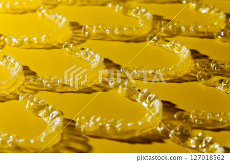 Orthodontic silicone aligner background. Advertisement of invisible braces retainer. Medical website concept. Pros and cons of aligners. Yellow saturated background 127018562