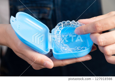 Hands of a Caucasian young woman holding dental aligners and a case for them 127018566