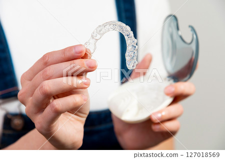 Hands of a Caucasian young woman holding dental aligners and a case for them 127018569