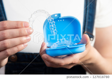 Hands of a Caucasian young woman holding dental aligners and a case for them 127018780