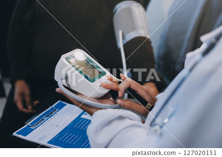 Doctor using Blood pressure monitor and stethoscope checking measuring arterial blood pressure on arm to a patient in the hospital, healthcare and medical concept 127020151