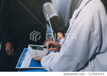 Doctor using Blood pressure monitor and stethoscope checking measuring arterial blood pressure on arm to a patient in the hospital, healthcare and medical concept 127020153