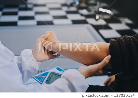 Orthopaedic doctor doing physical examination patient with wrist pain at the clinic. Physical therapist checks the patient wrist by pressing the wrist bone. 127020154