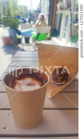 Disposable paper cup with coffee on a table in a cafe against the background of a sitting cat. Concept of a cat cafe, pet friendly cafe 127021480