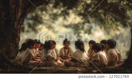 Elder teaches indigenous children their native language in a circle beneath a tree on a warm day 127021769