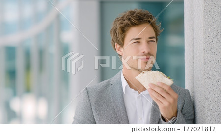 Office worker in casual business attire eats a wrap by a building entrance in natural light 127021812