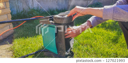 An elderly woman takes care of garden equipment - a lawn mower, wipes it. The concept of housework, gardening, gardening. An elderly woman takes care of garden equipment - a lawn mower, wipes it. The concept of housework, gardening, gardening. 127021993