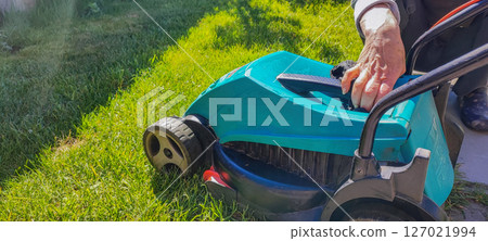 An elderly woman takes care of garden equipment - a lawn mower, wipes it. The concept of housework, gardening, gardening. 127021994