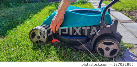 An elderly woman takes care of garden equipment - a lawn mower, wipes it. The concept of housework, gardening, gardening. 127021995