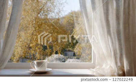 A gentle breeze moves the curtain as a comforting cup of tea sits on the windowsill, welcoming autumn 127022249