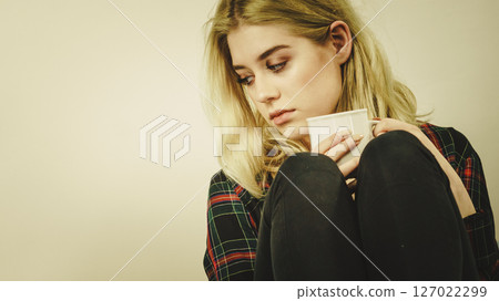 Sad lonely woman sitting on couch with mug Sad lonely woman sitting on couch with mug 127022299