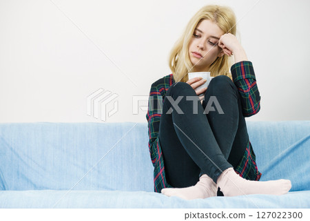 Sad lonely woman sitting on couch with mug Sad lonely woman sitting on couch with mug 127022300