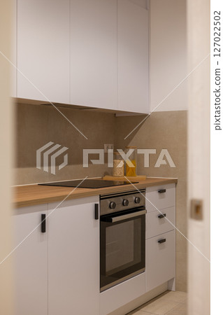 Minimalist kitchen with white cabinets, wood countertop, electric stove and jars of pasta and grains Minimalist kitchen with white cabinets, wood countertop, electric stove and jars of pasta and grains 127022502
