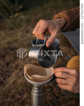 Close view of outdoor coffee brewing with metal cup pouring into paper filter funnel 127022504
