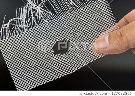 Hand holds damaged wire mesh with hole, possibly caused by rat. mesh is frayed and shows signs of wear, highlighting need for repair or replacement 127022835