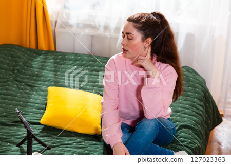 Mid shot of young female vlogger recording an online video while sitting on a cozy bed, offering social media tips. 127023363