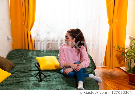 Passionate woman sitting on a bed, recording an insightful social media video for her followers. Wide shot Passionate woman sitting on a bed, recording an insightful social media video for her followers. Wide shot 127023364