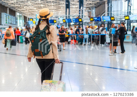 Back view of woman in an elegant suit holds luggage in airport. Copy space. A blurred departure lounge in the background. Web banner of trip and travel Back view of woman in an elegant suit holds luggage in airport. Copy space. A blurred departure lounge in the background. Web banner of trip and travel 127023386