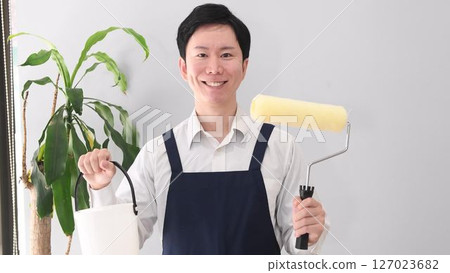 Smiling man in an apron holding a paint roller 127023682