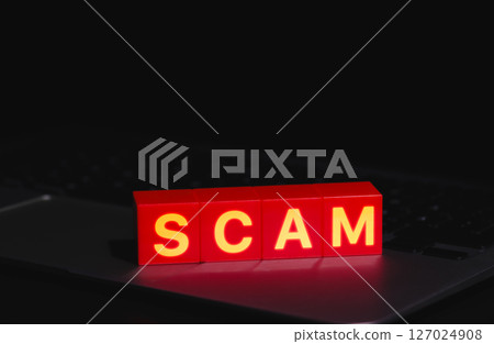Red Scam Blocks Highlighting Cyber Fraud. Spelling SCAM placed on laptop keyboard in dark environment, symbolizing cyber fraud, phishing, scammer, cybersecurity threats, and online deception risks. 127024908