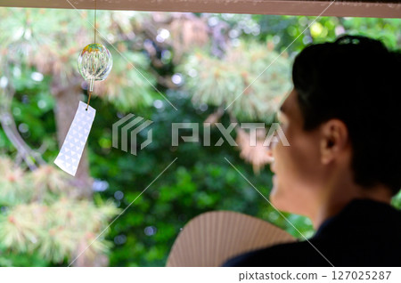A calm moment reflected in the back of a man gazing at wind chimes on a quiet veranda A calm moment reflected in the back of a man gazing at wind chimes on a quiet veranda 127025287