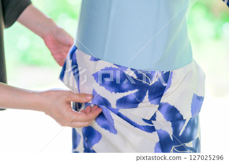 A scene of a person helping someone put on a yukata, conveying the warmth of their hands 127025296