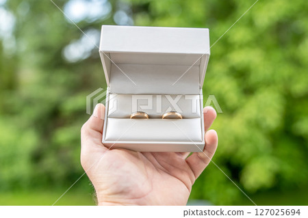 Elegant gold wedding rings lie among soft satin white ribbon. Front vertical view. Mockup for wedding postcard 127025694