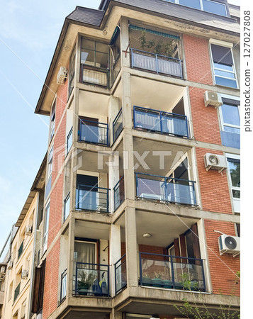 Residential building with balconies and red brick facade. Multi-story apartment structure featuring glass railings and air conditioning units. 127027808