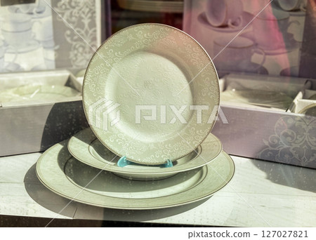 Ornate porcelain dinner plate on display. Embossed white plate with floral pattern showcased in shop window. Ornate porcelain dinner plate on display. Embossed white plate with floral pattern showcased in shop window. 127027821