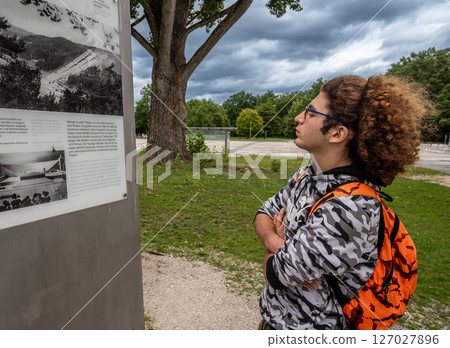 Nuremberg, Germany, August 3, 2023. A young Caucasian man with curly hair and glasses looks at information signs at the Nazi party rally site. Nuremberg, Germany, August 3, 2023. A young Caucasian man with curly hair and glasses looks at information signs at the Nazi party rally site. 127027896