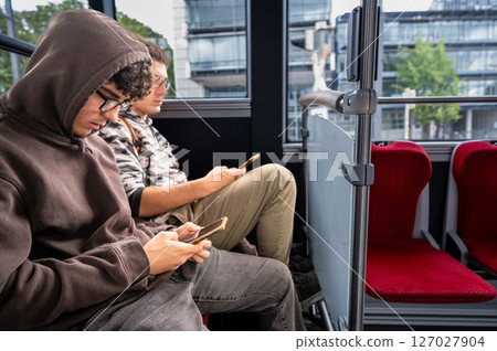 Two young people sitting on the bus talking using their cell phones. Concept of technology use by young people. Two young people sitting on the bus talking using their cell phones. Concept of technology use by young people. 127027904