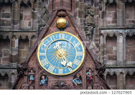 Nuremberg, Germany, August 3, 2023. Detail of the clock on the facade of the church Our Lady in the market square. Under the clock, protected by a net, the statues of some characters. 127027905