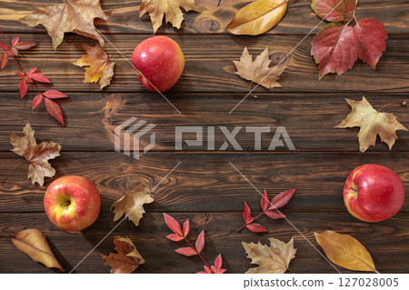 Bright red apples placed among colorful fallen leaves on dark wooden surface create warm autumn ambiance, highlighting vibrant seasonal hues and natural beauty of harvest time. Bright red apples placed among colorful fallen leaves on dark wooden surface create warm autumn ambiance, highlighting vibrant seasonal hues and natural beauty of harvest time. 127028005