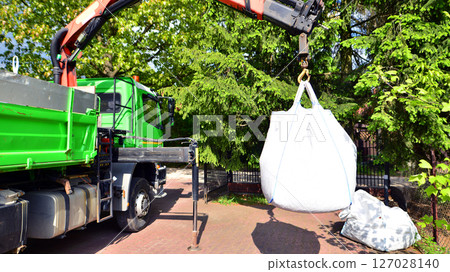 Crane with a big bag of stones. It is a white big bag with decorative stones for the property. 127028140