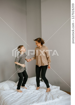 Mother and Son Joyfully Jumping on Bed at Home 127028209
