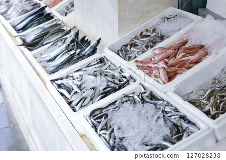 Vendors showcase a variety of fresh fish on ice at Greek fish market, early morning hours with glistening ice. 127028238